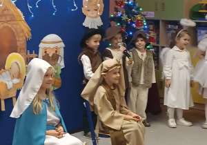 Dzieci przebrane za Maryję i Józefa siedzą przy kołysce. Chłopiec recytuje wiersz.