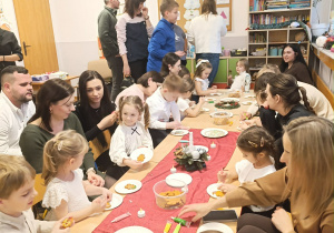 Dzieci wspólnie z rodzicami dekorują pierniki.