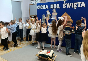 Na zdjęciu przedstawione są dzieci z rękoma uniesionymi do góry, podczas interpretacji ruchowej do piosenki.