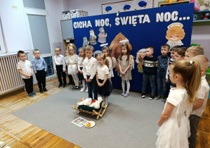 Chłopiec z dziewczynką stojący przed żłóbkiem recytują swoje role.