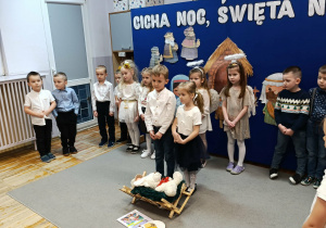 Chłopiec z dziewczynką stojący przed żłóbkiem recytują swoje role.