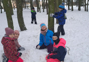Dziewczynki siedzą na śniegu w tle stoi dwóch chłopców.