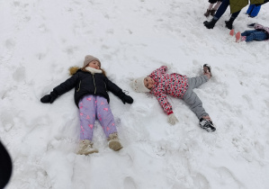 Dziewczynki robią orzełki na śniegu.