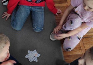 Czworo dzieci siedzi na dywanie, w środku leży ułożona przez nich matematyczna śnieżynka.