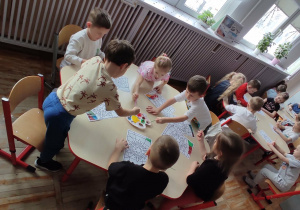 Dzieci siedzące przy stolikach wykonują pracę plastyczną z wykorzystaniem farby.
