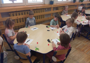 Zdjęcie przedstawia dzieci wyklejające kontur pingwina sztuką wydzieranki.