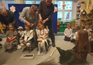 Babcie siedzą na krzesełkach i nawlekają nitkę na igłę.