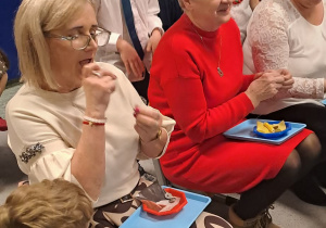 Babcie biorą udział w konkursie i przyszywają guziki do tkaniny.