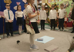 Dziewczynka w ręku trzyma mikrofon za nią stoją dzieci.