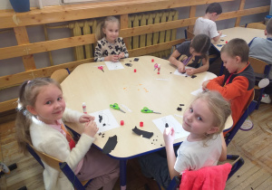 Zdjęcie przedstawia dzieci z grupy Odkrywcy wyklejające kontur pingwina sztuką wydzieranki.