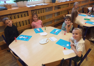 Zdjęcie przedstawia dzieci, wykonujące pracę plastyczną z bałwankiem.