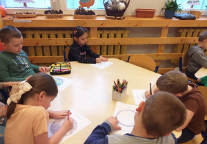 Zdjęcie przedstawia dzieci, dorysowujące dowolne elementy do konturu koła, tak aby stworzyć obraz własnego pomysłu.