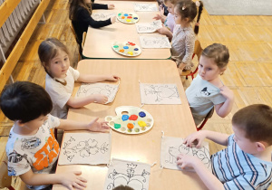 Dzieci siedzą przy stole oglądając szkic wzorów na swoich torebkach.