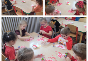 Dzieci z grupy słoneczka siedzą przy stolikach i wyklejają różowe serduszka czerwonymi kwadracikami.