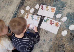 Chłopiec z dziewczynką z wykorzystaniem latarki dopasowują jajo do właściwego dinozaura.