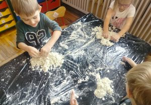 Chłopcy lepią w piasku kinetycznym.