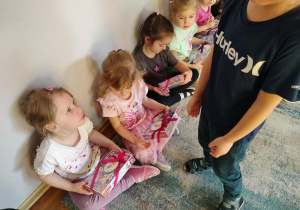 Chłopiec wręcza prezent dziewczynkom.