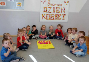 Dzieci siedzą dookoła wspólnie wykonanej pracy - wazonu z kwiatami.