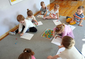 Dzieci układają kontur figur z kolorowych koralików.