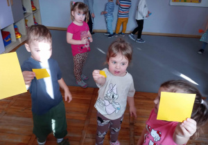 Przedszkolaki pokazujące żółte kwadraty trzymane w dłoniach.
