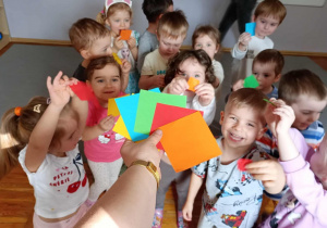 Dzieci pokazują nauczycielce różnokolorowe kwadraty w dłoniach.