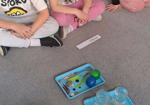 Dzieci siedzą na dywanie przed nimi leżą przedmioty.