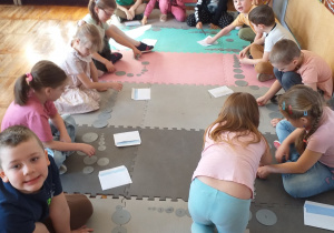 Dzieci układają kamienie w postaci ponumerowanych szarych kół różnej wielkości w kolejności od najmniejszego do najmniejszego.