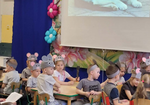 Dzieci siedzą przy stolikach, w tle kot domowy.