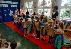 Dzieci stoją na czerwonym dywanie i prezentują swoje stroje.