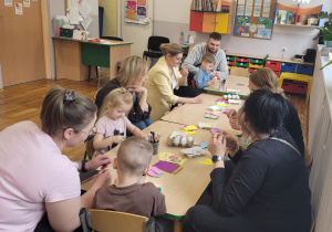 Słoneczka z rodzicami siedzą przy stoliku i wykonują świąteczne ozdoby.