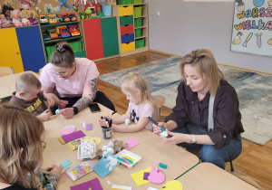 Słoneczka z rodzicami siedzą przy stoliku i wykonują świąteczne ozdoby.