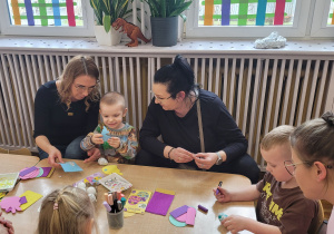 Słoneczka z rodzicami siedzą przy stoliku i wykonują świąteczne ozdoby.