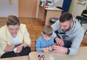 Chłopiec z rodzicami siedzi przy stoliku i wykonuje świąteczne ozdoby.