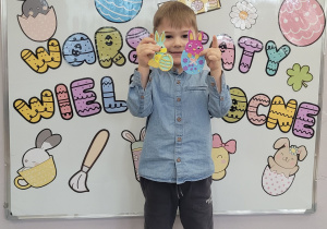 Chłopiec prezentuje na tle tablicy z dekoracją wykonane ozdoby.