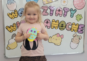 Dziewczynka prezentuje na tle tablicy z dekoracją wykonane ozdoby.