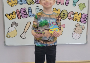 Chłopiec prezentuje na tle tablicy z dekoracją wykonane ozdoby.