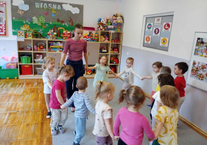 Przedszkolaki trzymają się za dłonie i tańczą w kole.