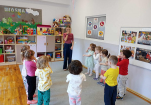 Starsza dziewczynka stoi w kole i pokazuje gestem słowa piosenki.