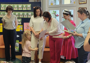 Wręczenie dziewczynce dyplomu i nagrody za udział w konkursie plastycznym.