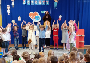 Dzieci wykonują wraz z misiem muzyczną gimnastykę.