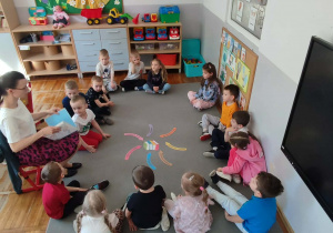 Dzieci siedzące na dywanie słuchają bajek czytanych przez nauczyciela.