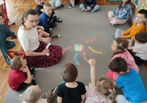 Dzieci siedzące na dywanie biorą aktywny udział w dyskusji dotyczącej korzyści płynących z czytania i słuchania książek.