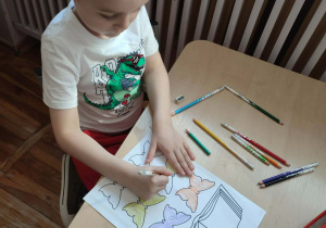 Chłopiec siedzący przy stoliku koloruje kredkami motylki.