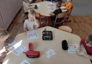 Dzieci siedzące przy stolikach wykonują pracę plastyczną związaną z obchodami Dnia Książki.