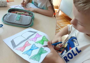 Chłopiec wycina z papieru pokolorowane motylki.