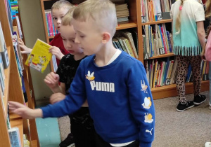 Chłopiec będący w szkolnej bibliotece wyjmuje z półki książkę, która go zainteresowała.