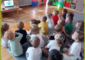 Dzieci siedzą na dywanie i oglądają film edukacyjny dotyczący ekologii.