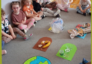 Dzieci siedzą dookoła posegregowanych śmieci.