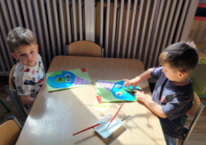 Chłopcy siedzą przy stoliku i wykonują pracę plastyczną.