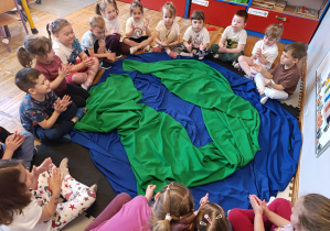 Dzieci siedzą wokół utworzonej z materiałów planety Ziemi.